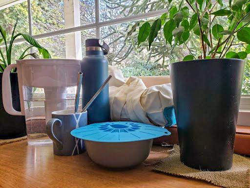 An assortment of reusable items and plants sit by a window.