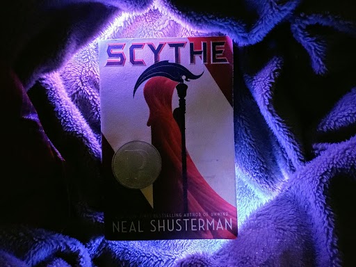 A copy of Scythe enjoys a luxurious existence upon a fluffy blanket, surrounded by lights.