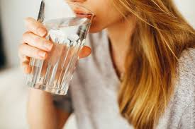 A woman drinks water out of a glass. Hydration has many important benefits that are often overlooked.
