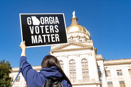 A protester holds up a sign in front of the Georgia capitol building. A recently passed bill has drawn mixed reactions, with proponents saying it makes it easier to vote and critics saying the opposite.